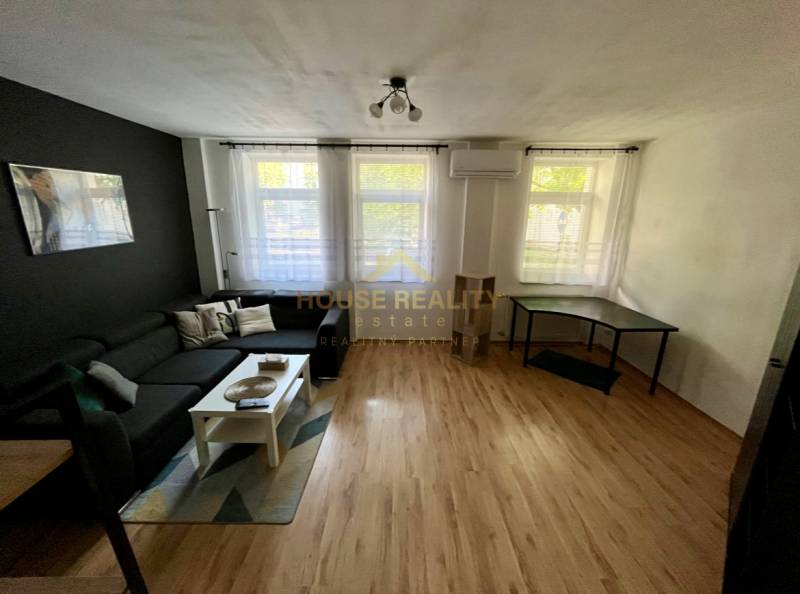 Wohnzimmer mit schwarzem Sofa, weißem Tisch und Schreibtisch in einer Zweizimmerwohnung.