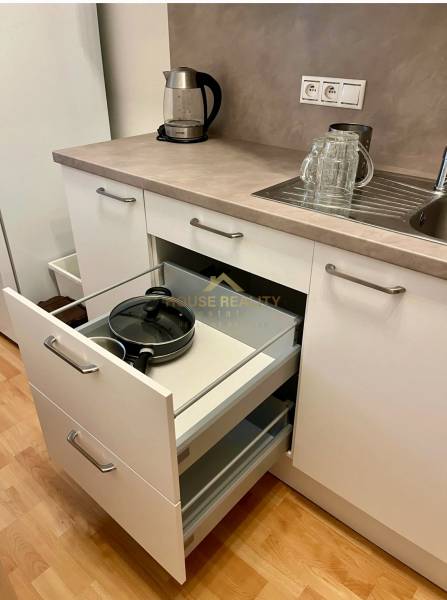 Küche mit weißen Schränken, offener Schublade, Spüle und Wasserkocher in einer Zweizimmerwohnung.