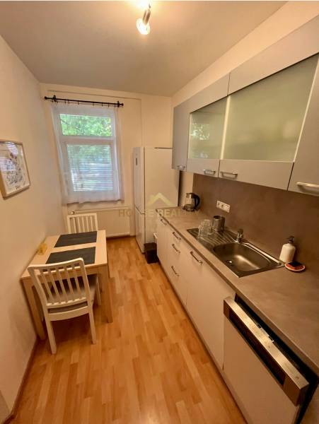 Küche in einer 2-Zimmer-Wohnung mit Esstisch, weißen Schränken und Geräten.