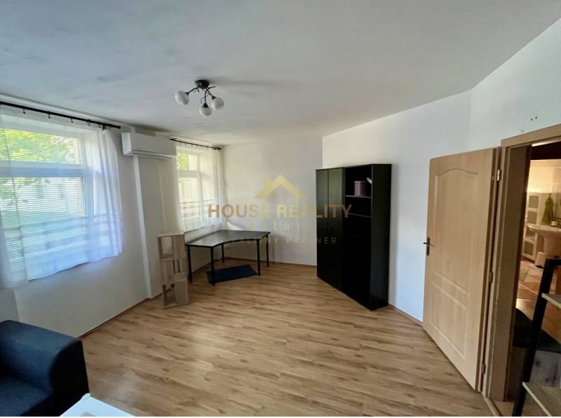 Ein Zimmer in einer 2-Zimmer-Wohnung mit Holzboden, Klimaanlage, Möbeln und Fenstern mit Rollläden.