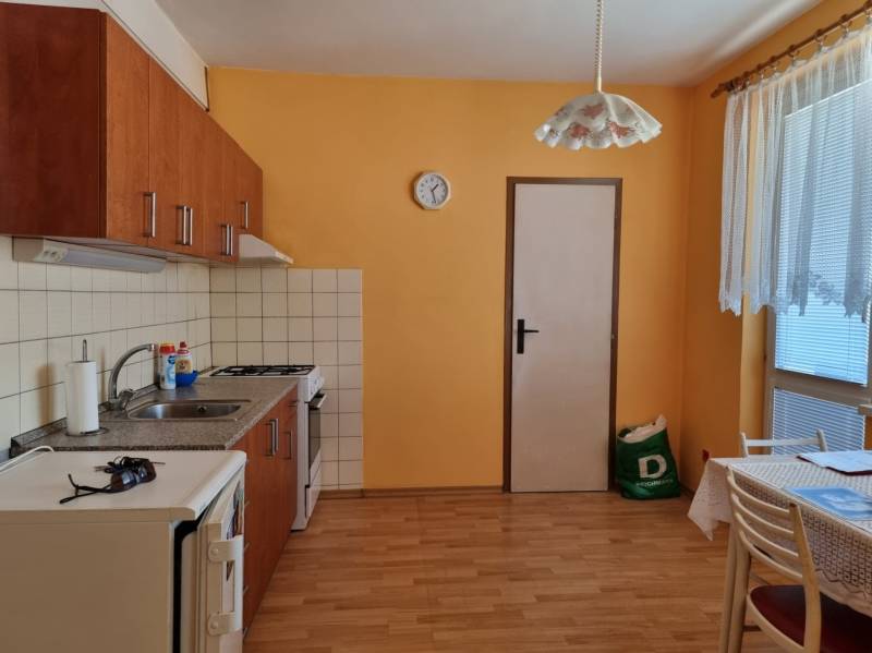 Eine Küche in einer 2-Zimmer-Wohnung mit orangefarbenen Wänden, Holzboden und einem Esstisch.