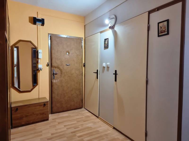 Flur in einer 2-Zimmer-Wohnung mit Holzmöbeln, Spiegel und Sicherheitstür.