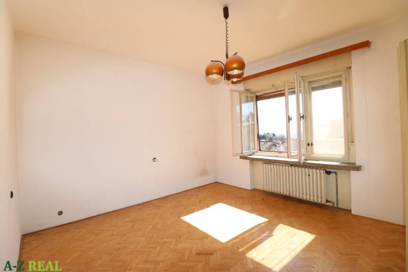 Ein Zimmer in einem Einfamilienhaus mit Holzboden, Heizkörper und offenem Fenster.