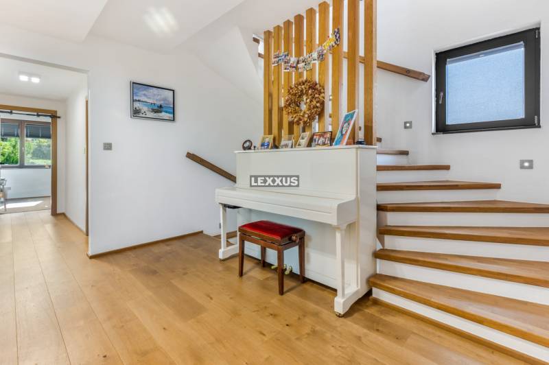 Innenraum eines Einfamilienhauses mit Treppe, weißem Klavier und Holzboden.