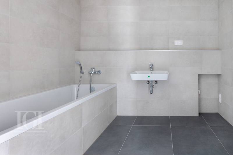 Badezimmer mit Badewanne und Waschbecken in einer 3-Zimmer-Wohnung mit neutralen Fliesen.