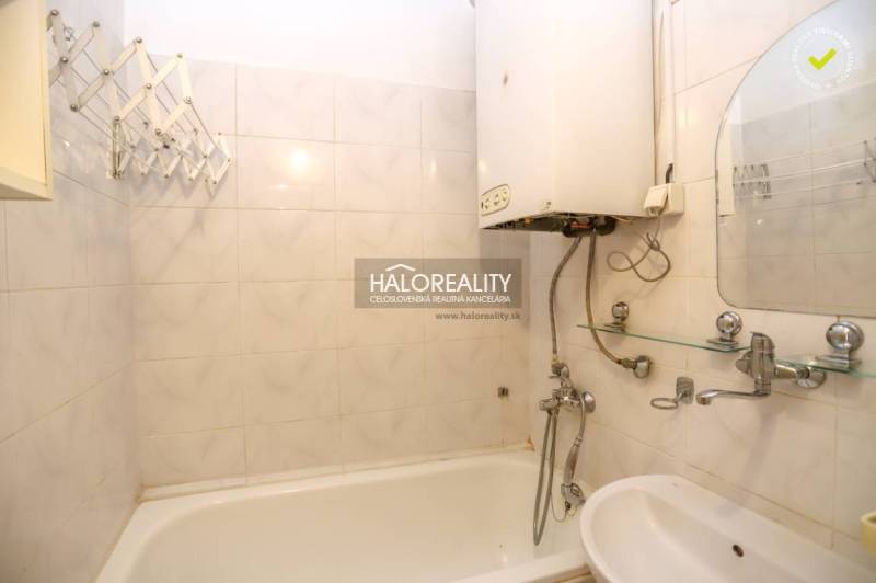 Badezimmer mit Badewanne und Boiler in einer 3-Zimmer-Wohnung, weiße Fliesen, Waschbecken.