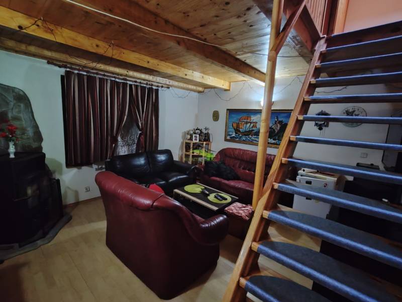 Interieur einer Hütte mit Holzbalkendecke, Sofas und einer Treppe, die in den oberen Stock führt.