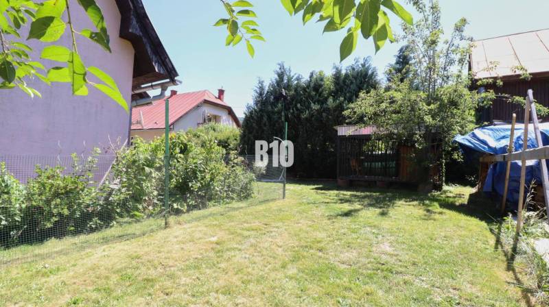 Der Garten beim Einfamilienhaus in Podhradí, mit Rasen, Sträuchern und Bäumen, der Zaun ist sichtbar.
