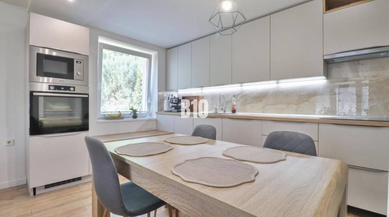 Küche in einem Einfamilienhaus mit Esstisch, eingebauten Geräten und großem Fenster.
