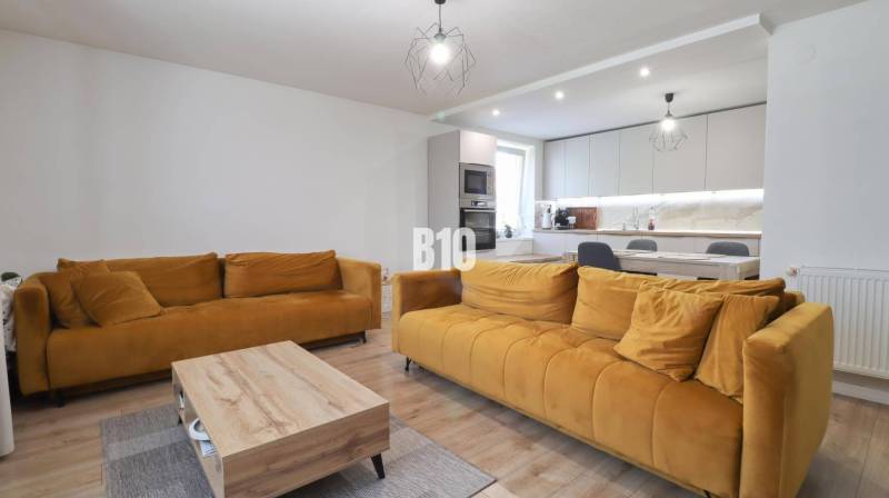Wohnzimmer in einem Einfamilienhaus mit senffarbenen Sofas und Küchenzeile.