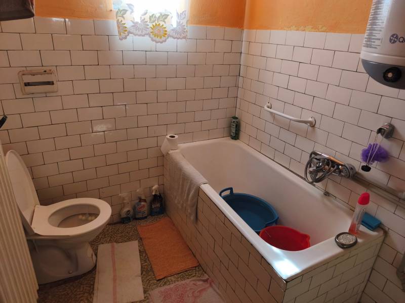 Badezimmer in einem Einfamilienhaus mit weißen Fliesen, Badewanne und Toilette.