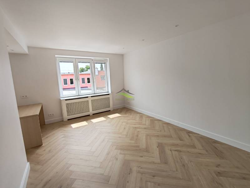 Ein Zimmer mit Holzboden und einem großen Fenster in einer 2-Zimmer-Wohnung.