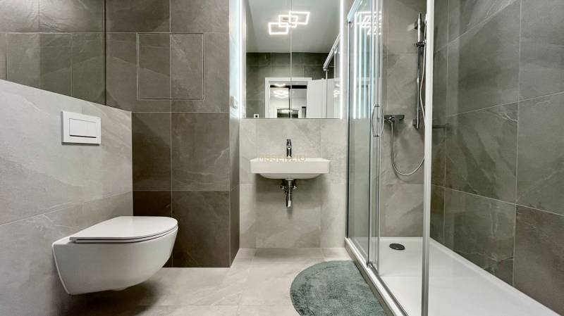Badezimmer in einer 2-Zimmer-Wohnung mit Toilette, Dusche und Waschbecken mit Fliesen.