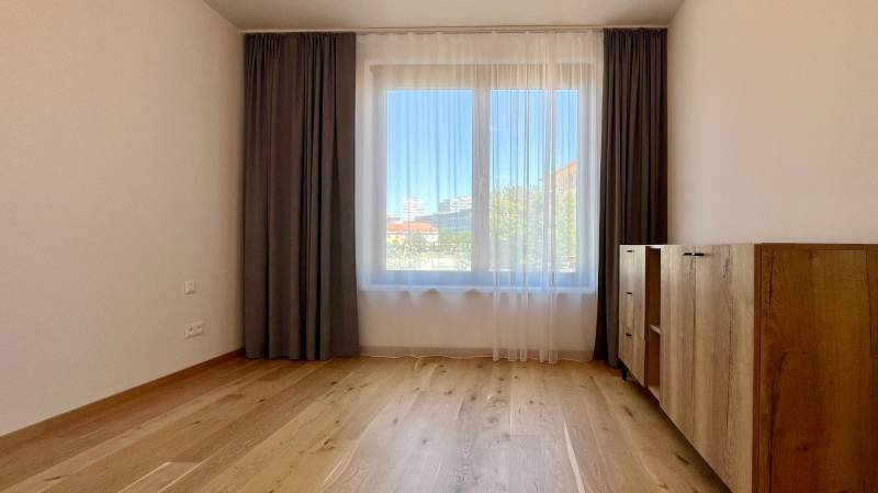 Geräumiges Zimmer mit Holzboden, Vorhängen und Kommode in einer 2-Zimmer-Wohnung.