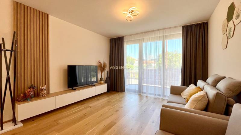 Wohnzimmer in einer Zweizimmerwohnung mit Sofa, Fernseher und Holzboden.
