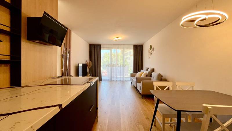 Wohnzimmer in einer Zweizimmerwohnung mit Küchenzeile, Holzboden und großem Fenster.