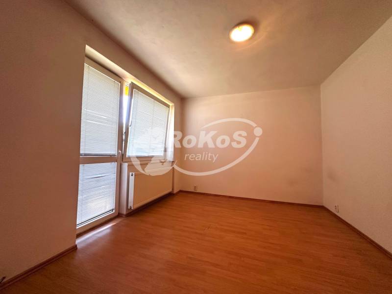 Ein Zimmer mit Holzboden, Heizkörper und Fenster mit Rollläden in einer 3-Zimmer-Wohnung.