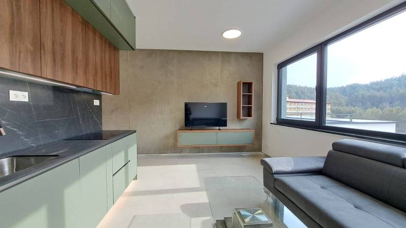 Küchenzeile mit Fernseher und Sofa in einer 2-Zimmer-Wohnung mit großem Fenster.