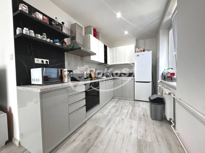 Küche in einer 2-Zimmer-Wohnung mit weißen Möbeln, Geräten und schwarzem Fliesenspiegel.
