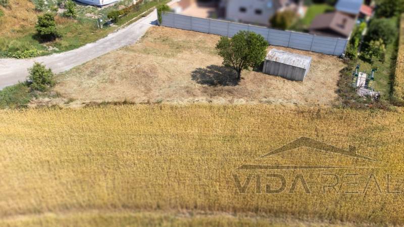 Ein ruhiges Grundstück zum Wohnen in Dunajská Lužná, mit einem Unterstand und einem Baum.