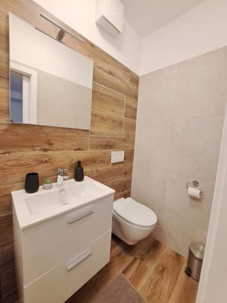 Badezimmer in einer 2-Zimmer-Wohnung mit Holz- und Keramikverkleidungen, mit Waschbecken und Toilette.