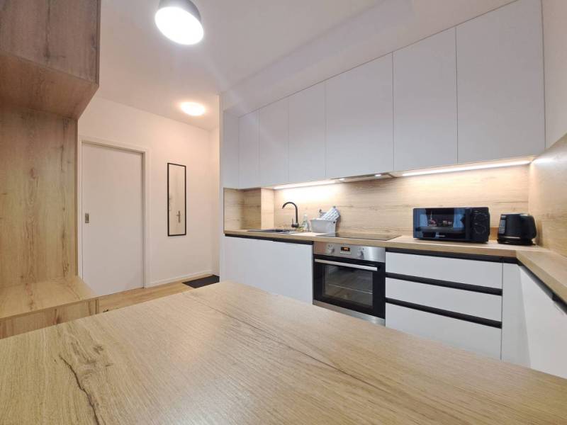 Küche in einer 2-Zimmer-Wohnung mit einer Arbeitsplatte aus Holz und weißen Schränken.