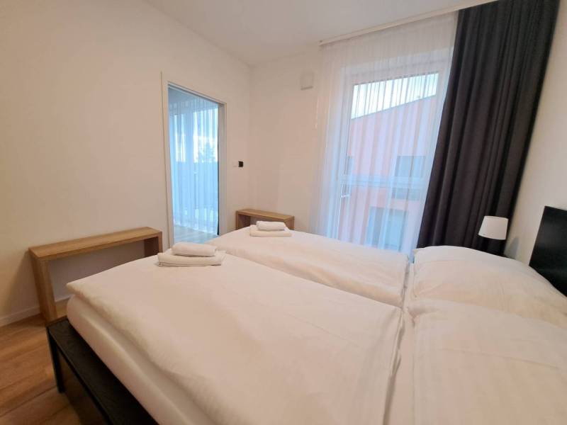 Schlafzimmer in einer Zweizimmerwohnung mit zwei Betten, Holztischen und Vorhängen.