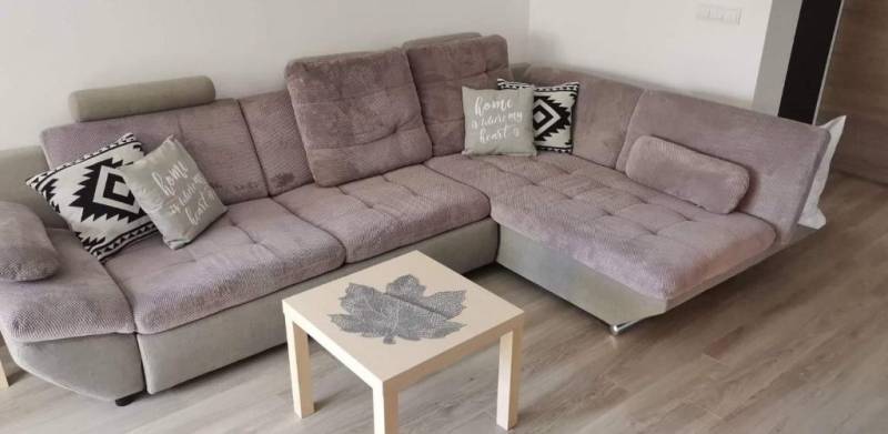 Bequeme Sitzgarnitur in einer 3-Zimmer-Wohnung, ergänzt durch Kissen und einen Tisch mit Blattmotiv.
