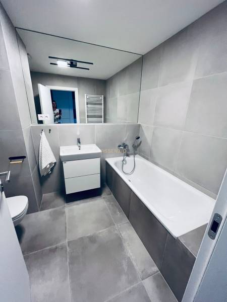 Badezimmer mit Badewanne, Waschbecken und Spiegel in einer 2-Zimmer-Wohnung mit Fliesen.