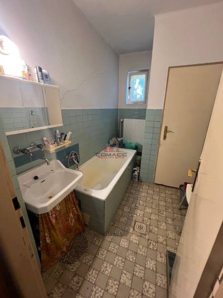 Ein Badezimmer in einem Einfamilienhaus mit einer alten Badewanne, einem Waschbecken und Fliesen.