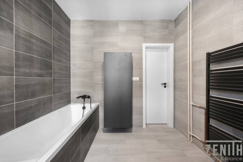 Badezimmer mit Badewanne, grauen Fliesen und schwarzen Accessoires in einer 3-Zimmer-Wohnung.