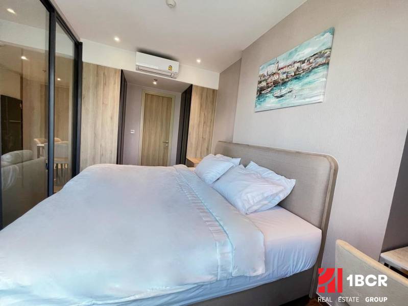 Helles Schlafzimmer mit großem Bett in einer 2-Zimmer-Wohnung, umgeben von Holzelementen.