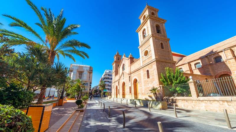 Calle Campoamor 12 in Torrevieja mit einer Kirche und Palmen an einem sonnigen Tag.