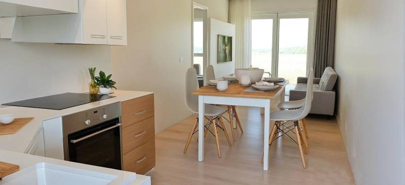 Esstisch mit Stühlen und Küche in einer 3-Zimmer-Wohnung mit heller Dekoration.