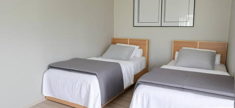 Zwei Einzelbetten mit grauen Decken in einer 3-Zimmer-Wohnung.