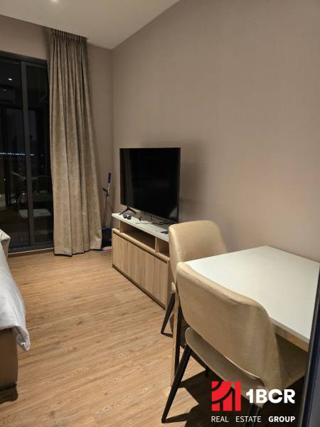 Interieur einer Einzimmerwohnung mit Tisch, Stühlen, Fernseher und Vorhängen.