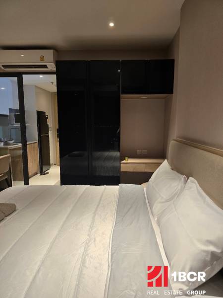Schlafzimmer mit weißem Bett und schwarzem Schrank, neben der Küchenzeile.