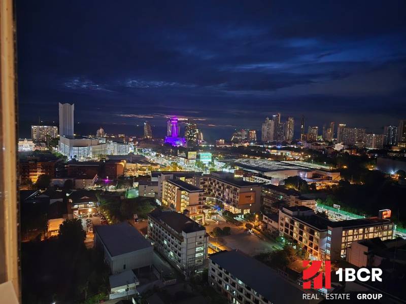 Nächtlicher Blick auf die Stadt Pattaya mit beleuchteten Gebäuden und Silhouetten am Horizont.