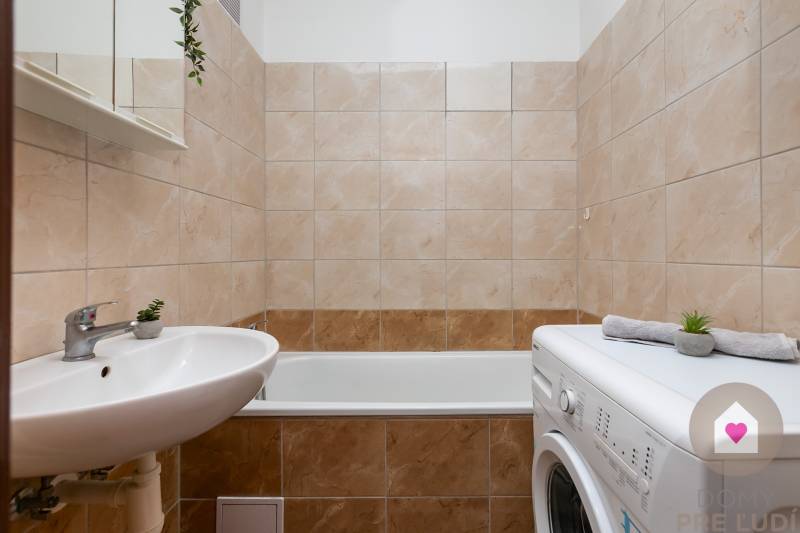 Badezimmer mit Badewanne, Waschbecken und Waschmaschine in einer Einzimmerwohnung.