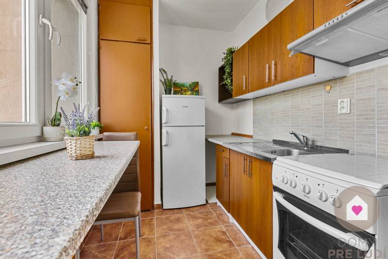 Kompakte Küche mit braunen Schränken und weißen Geräten in einer Einzimmerwohnung.