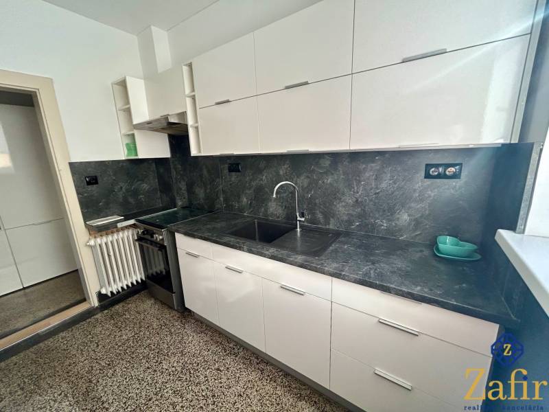 Küche mit weißen Schränken und grauer Arbeitsplatte in einer 3-Zimmer-Wohnung.
