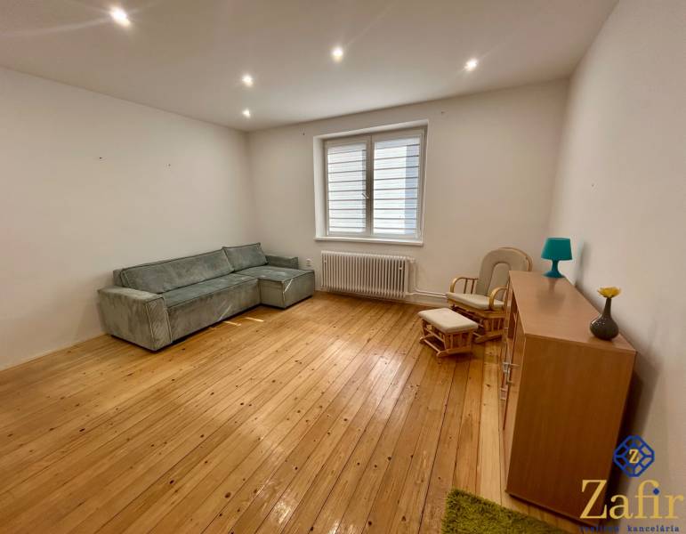 Wohnzimmer mit Holzboden, grauem Sofa und Sessel in einer 3-Zimmer-Wohnung.