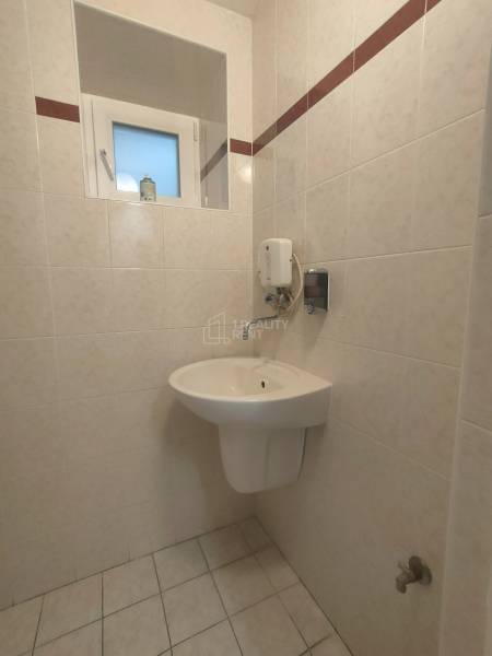 Badezimmer mit Waschbecken, Fenster und Seifenspender in einem gefliesten Bereich von Geschäftsräumen.