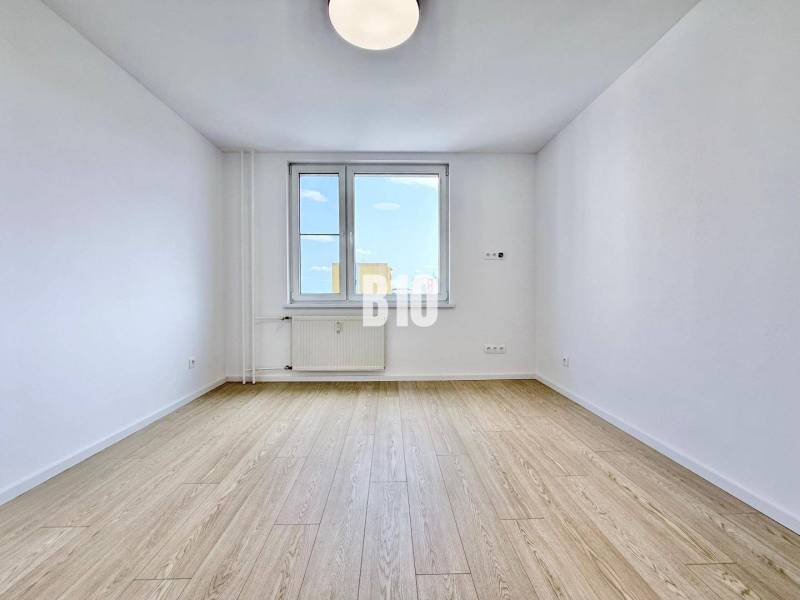 Helles Zimmer mit Holzboden und großem Fenster in einer 3-Zimmer-Wohnung.