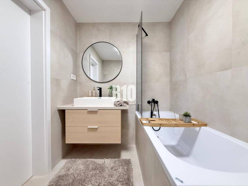 Ein Badezimmer in einer 3-Zimmer-Wohnung mit Badewanne, Spiegel und Holzzubehör.