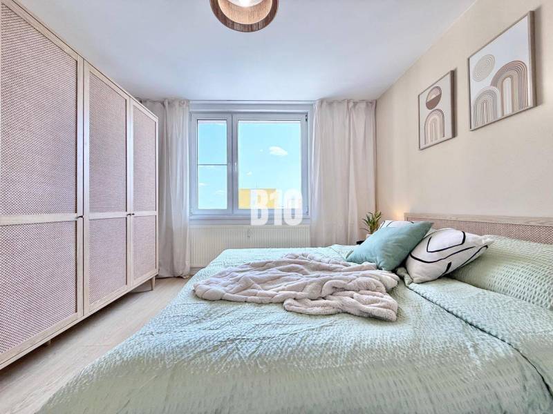 Helles Schlafzimmer in einer 3-Zimmer-Wohnung mit großem Bett, Schrank und dekorativen Bildern.