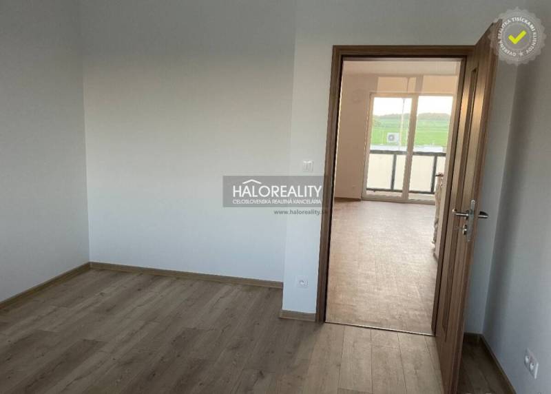 Ein Zimmer mit weißen Wänden und Türen zu einem hellen Raum in einer Zweizimmerwohnung.