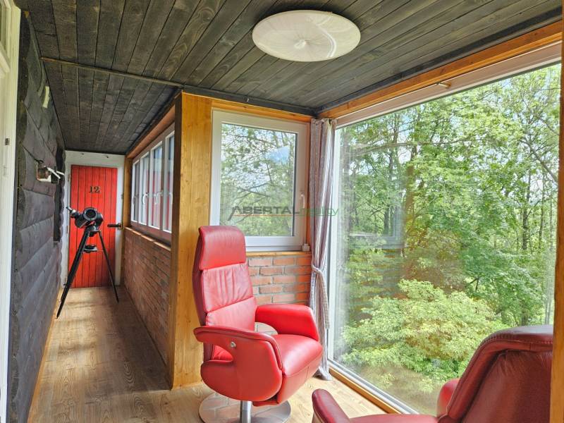 Ein Einfamilienhaus mit verglaster Veranda, roten Sesseln, Teleskop und Blick auf den Wald.