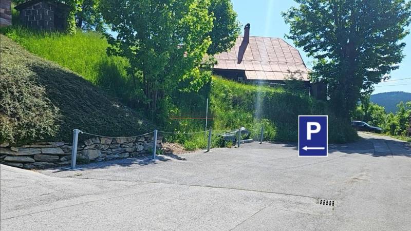 Parkplatz in der Donovaly-Straße in der Stadt Donovaly bei Einfamilienhäusern, mit Bäumen und Gras.