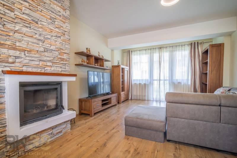 Wohnzimmer in einer Ferienwohnung mit Kamin, Sofa und großem Fenster.